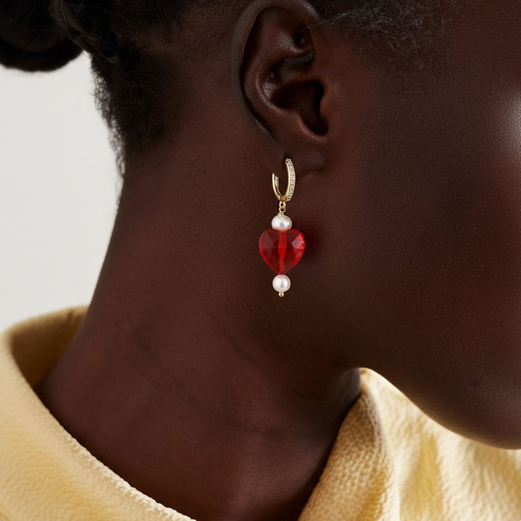 Close-up of an ear wearing a red and pearl earring with a neutral background