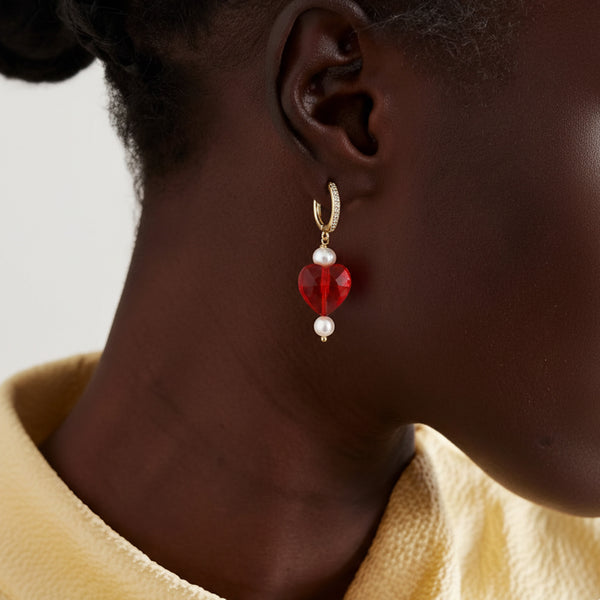 Close-up of an ear wearing a red and pearl earring with a neutral background